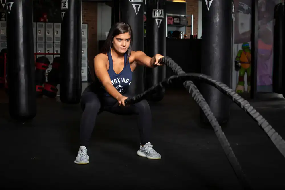 Trainer guiding a client through battle ropes in a local park